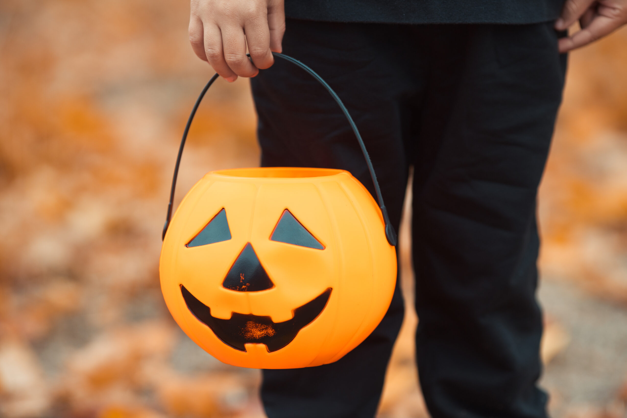 Close up kid's hand hold a halloween candy bucket in pumpkin shape for trick or treat game. Celebrate all saints day with jack lantern.